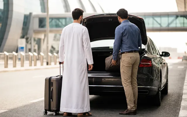 Driver loading a traveller's luggage into their own car at Dubai airport curbside