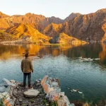 Scenic sunset view of Al Rafisah Dam in Khor Fakkan with kayaking activities and reflections of the Hajar Mountains on the water